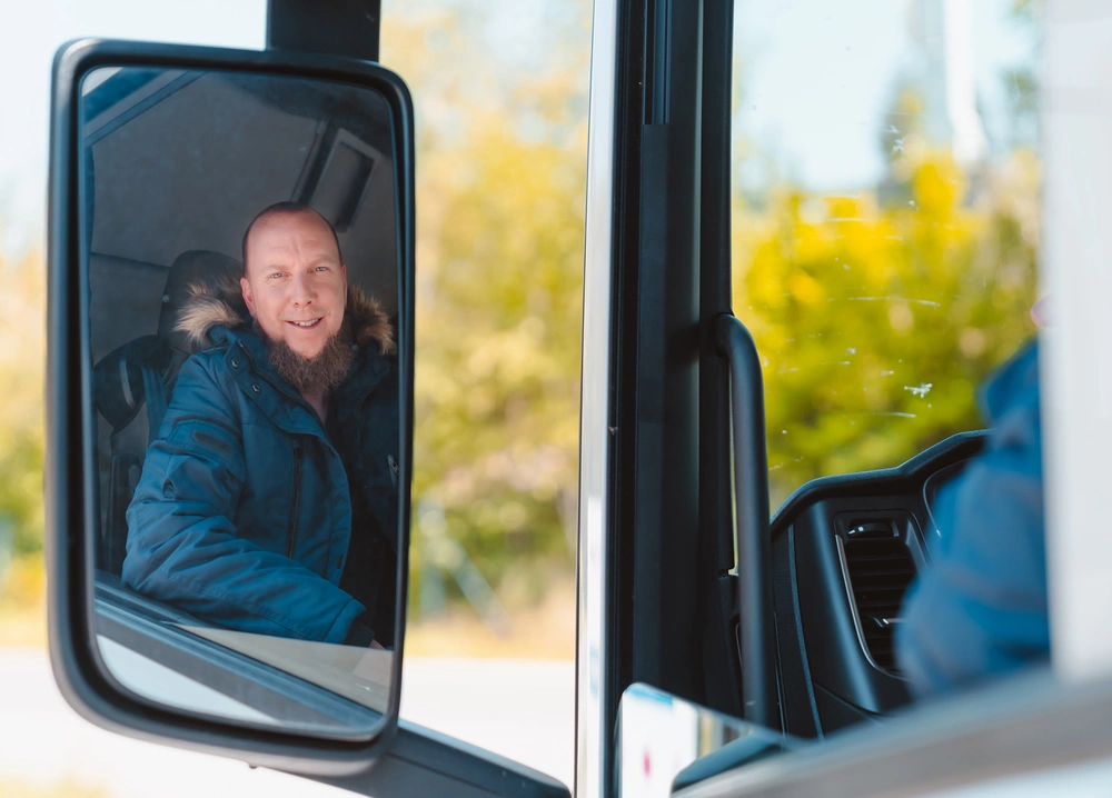 [Translate to English:] LKW-Fahrer im Seitenspiegel - lächelt in die Kamera 